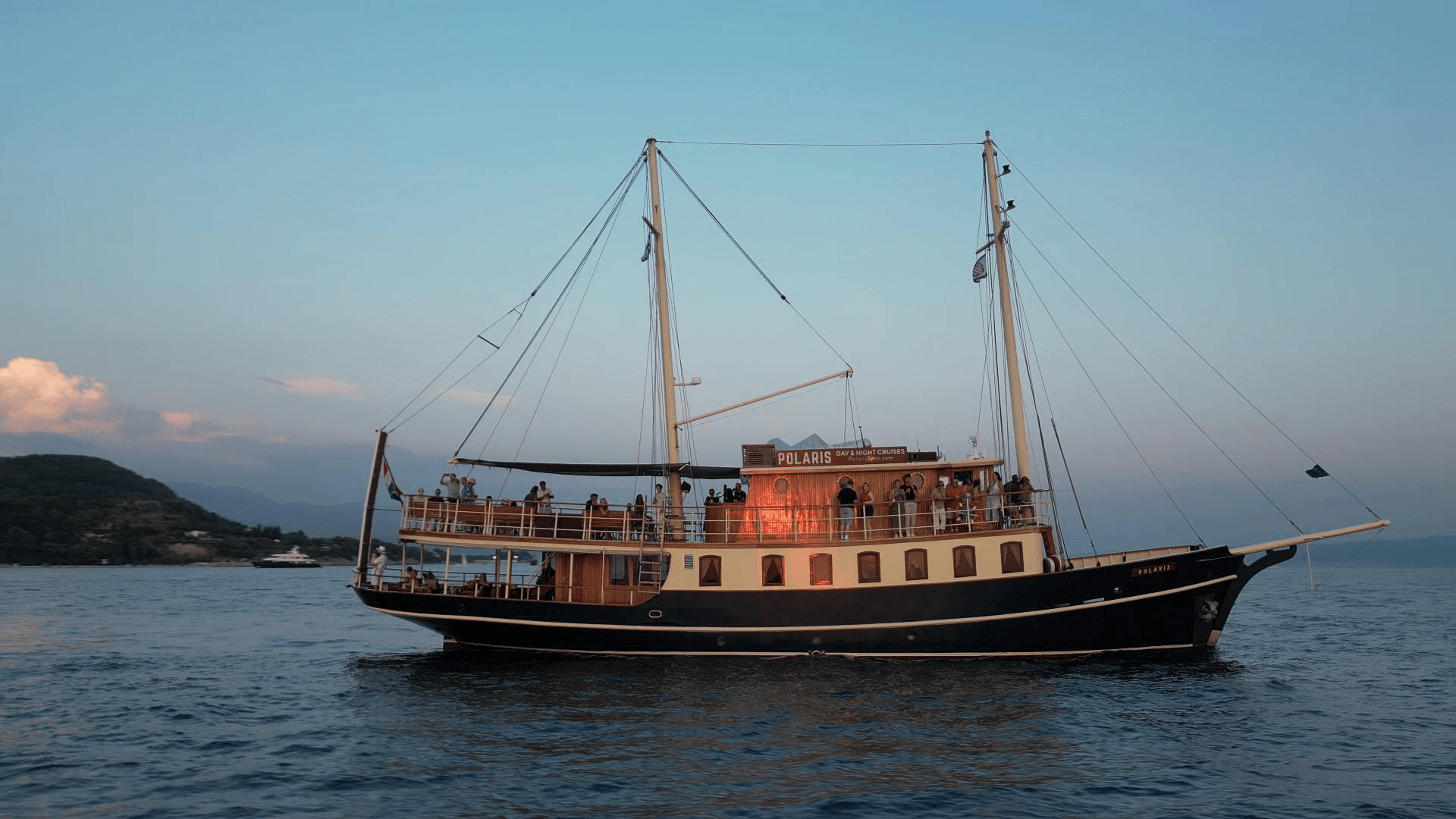 The yacht Polaris at dusk with guests on deck under its glowing Day & Night Cruises sign