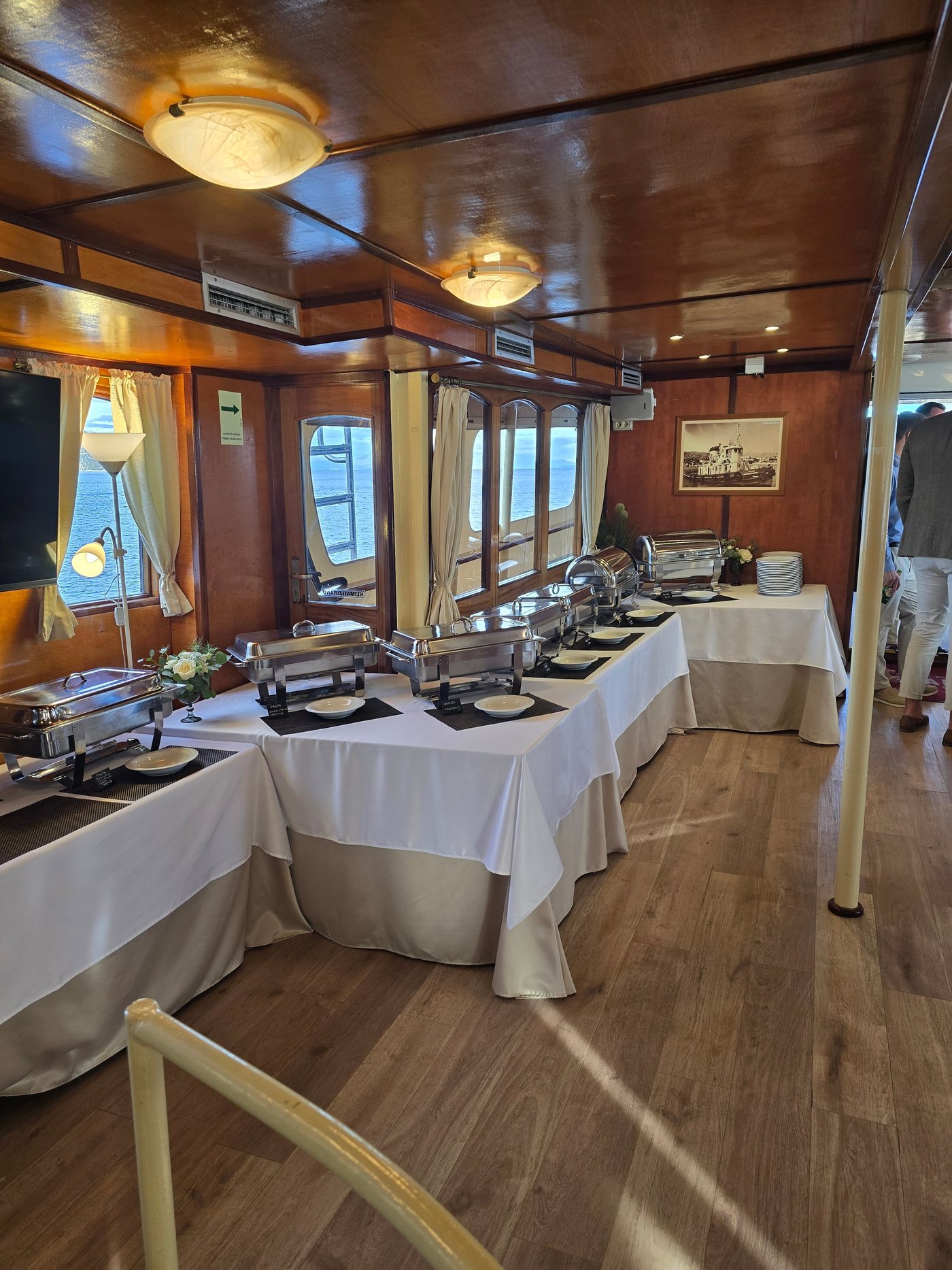 Buffet-style catering set up with chafing dishes in the air-conditioned indoor saloon of Polaris, with Adriatic sea views through the windows