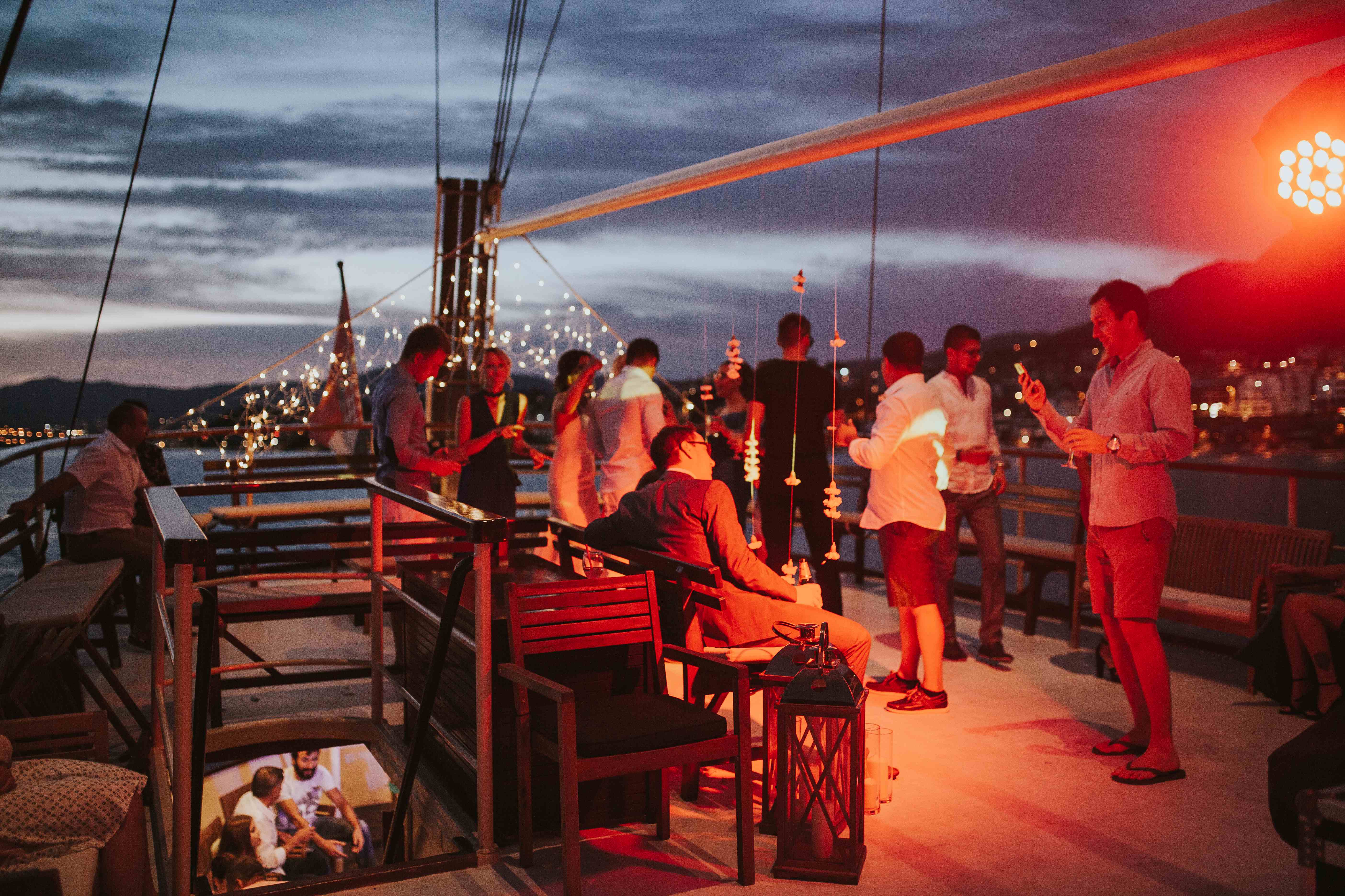 Guests mingling with drinks on the deck of Polaris under string lights at dusk