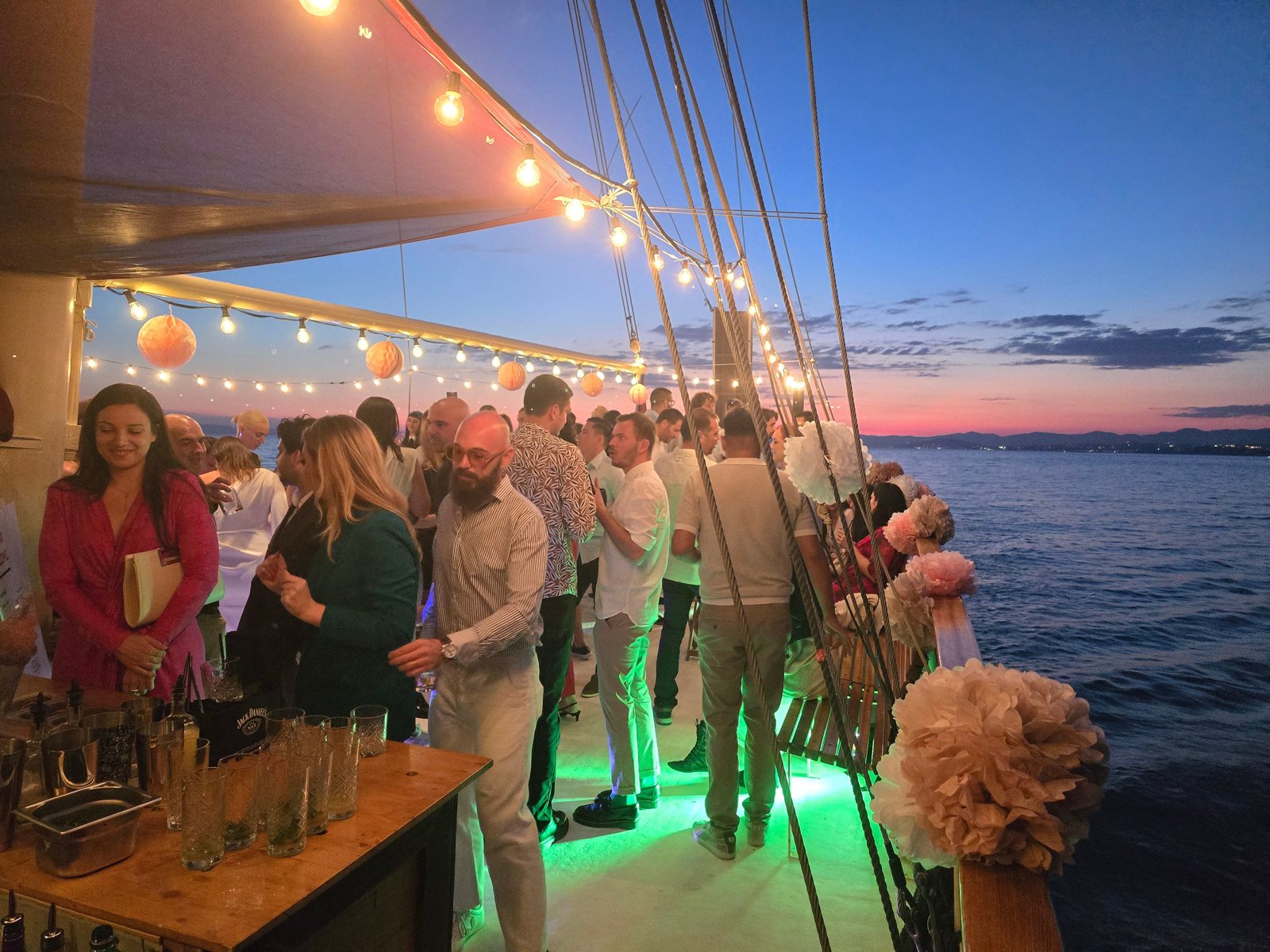 Guests networking with cocktails under string lights on the deck of Polaris at dusk