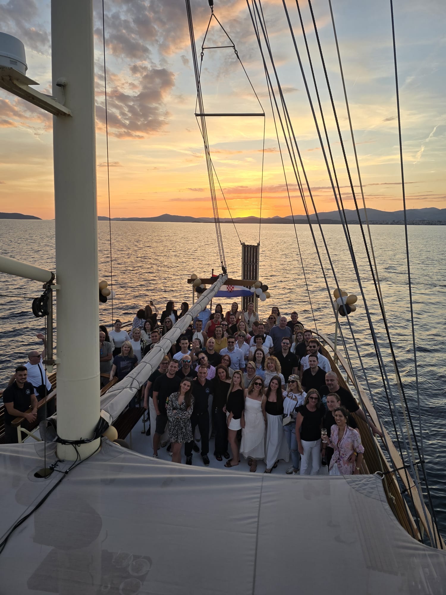 A large group of guests gathered on the deck of the yacht Polaris for a private celebration at golden-hour sunset over the Adriatic