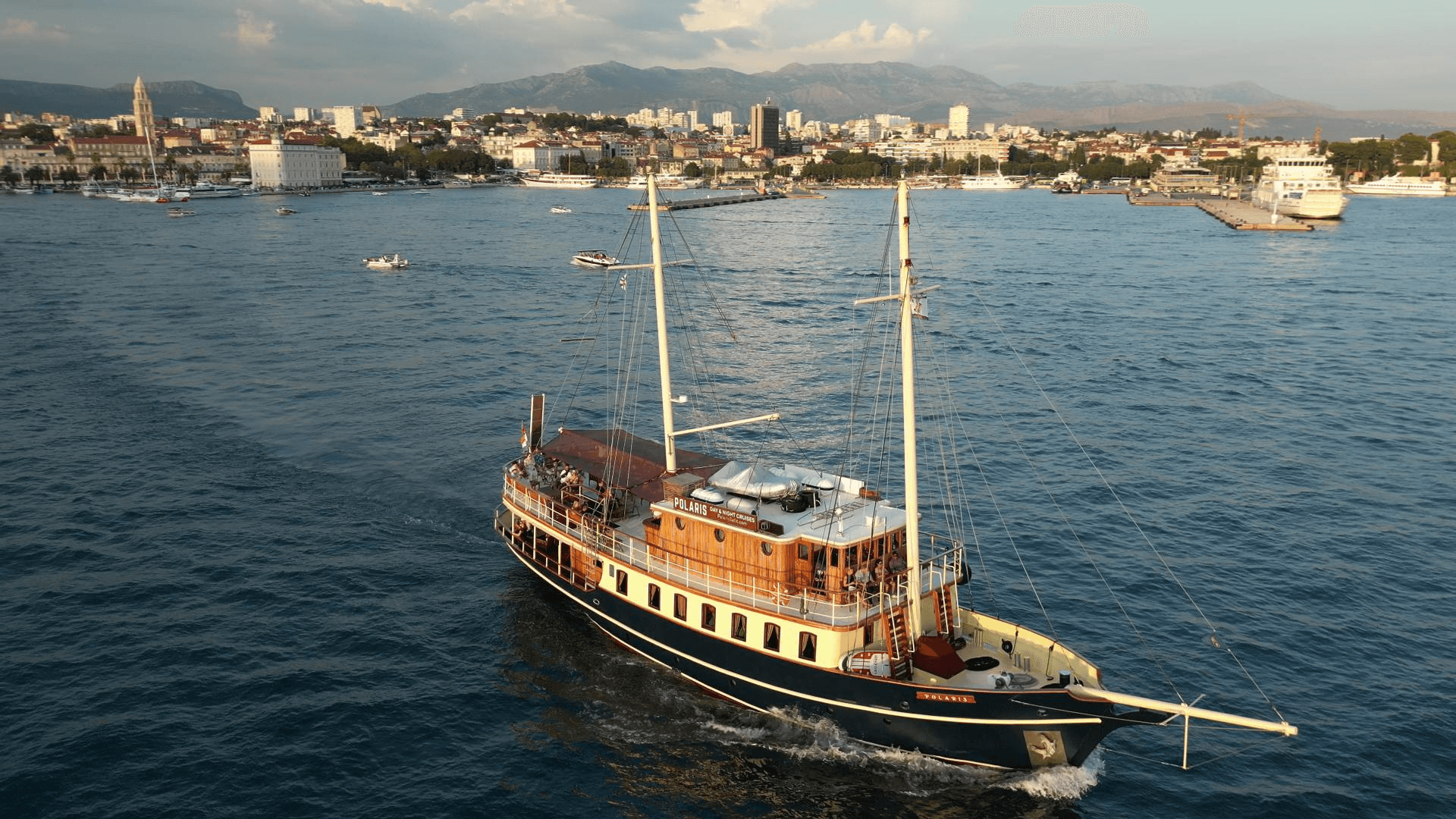 Aerial view of the yacht Polaris cruising across Split harbour with the city and mountains behind