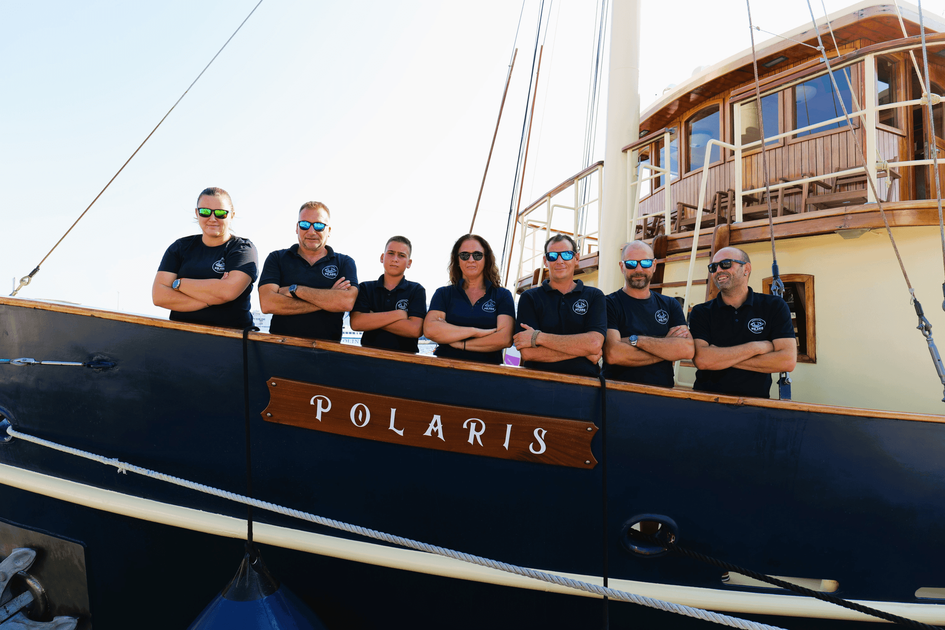 The Polaris crew posing together along the rail of the restored yacht at the dock