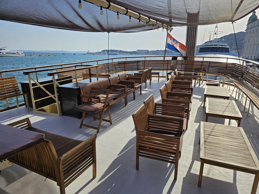 Das offene Sonnendeck der Polaris mit Teakstühlen, Bänken und Tischen unter einem Sonnendach mit Blick auf den Hafen von Split