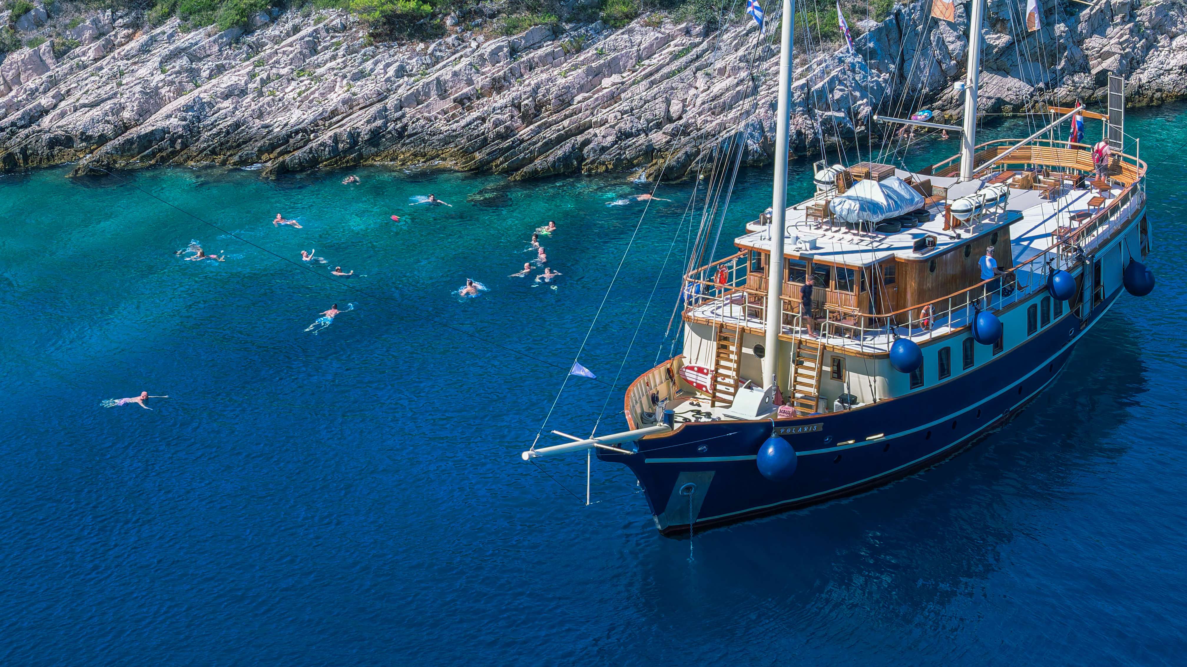 Guests swimming and snorkeling in a secluded turquoise cove around the anchored yacht Polaris on the Adriatic