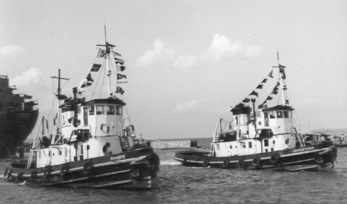 Die Schlepper Ryhope und Grangetown mit Signalflaggen über die Toppen geflaggt im Hafen neben einem größeren Schiff