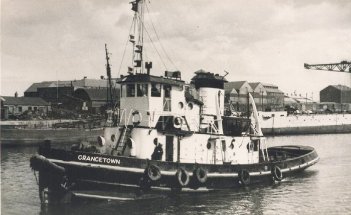The tug Grangetown moored in a dock basin with warehouses and a large crane on the quayside behind her