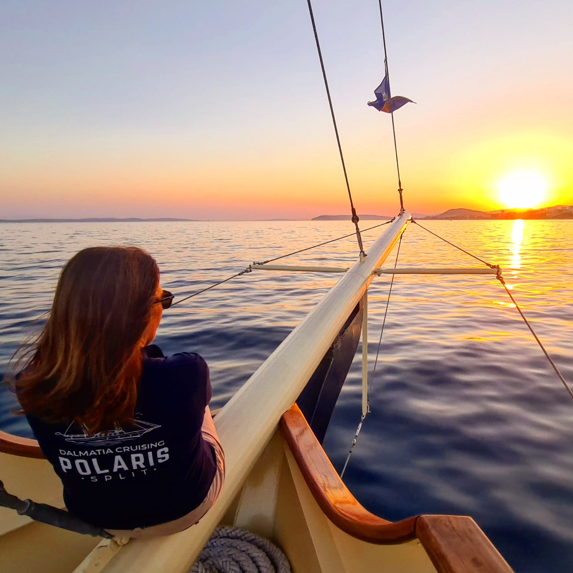 Guest at the bow of Polaris watching the sun set over the bowsprit