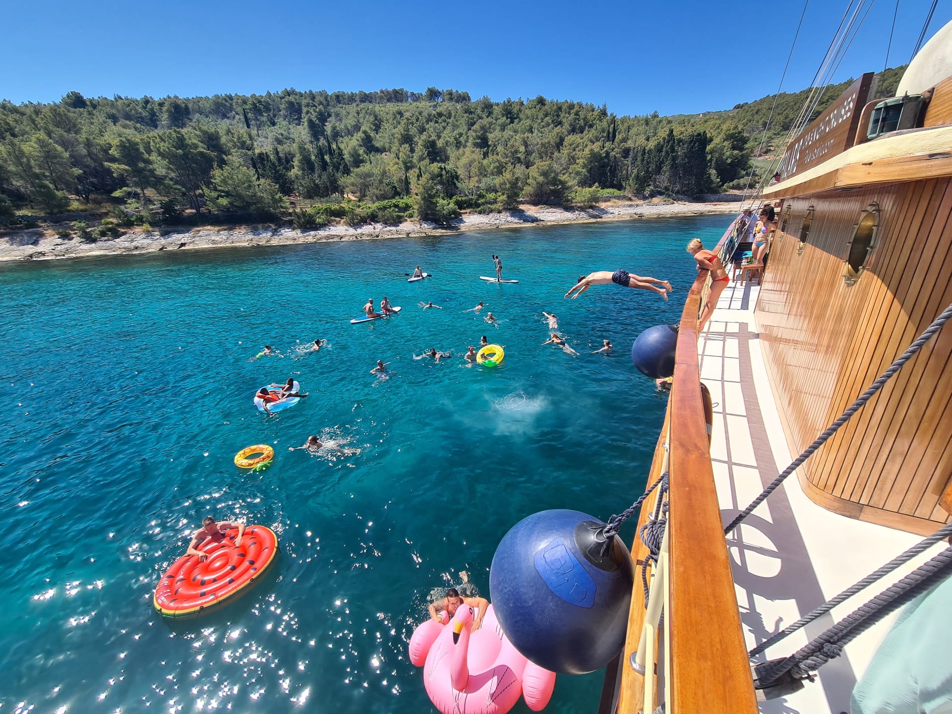 Gäste schwimmen zwischen bunten Schwimmtieren neben der Polaris in einer türkisfarbenen Bucht