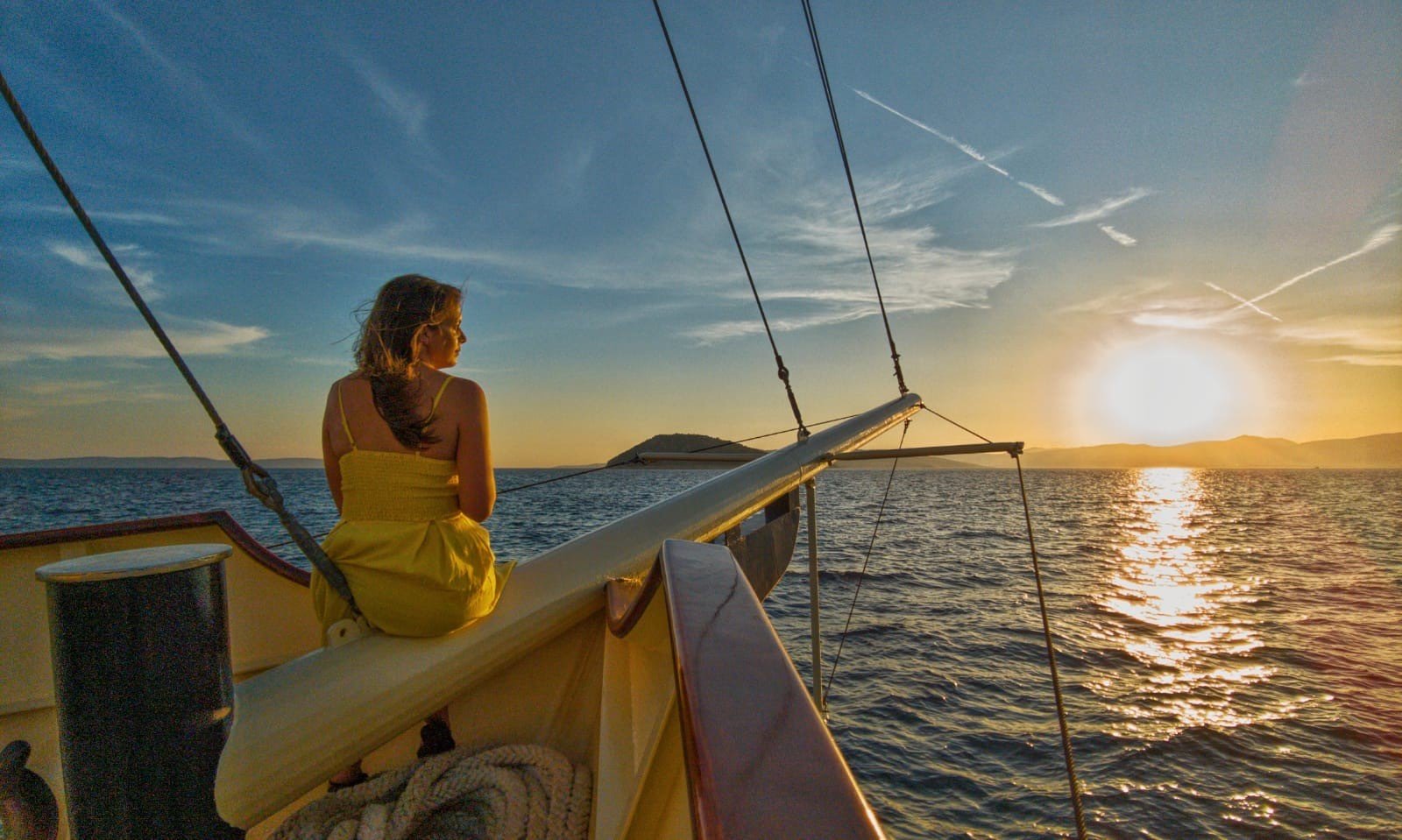 A woman in a yellow dress on the bow of Polaris watching a golden sunset over the Adriatic near Split