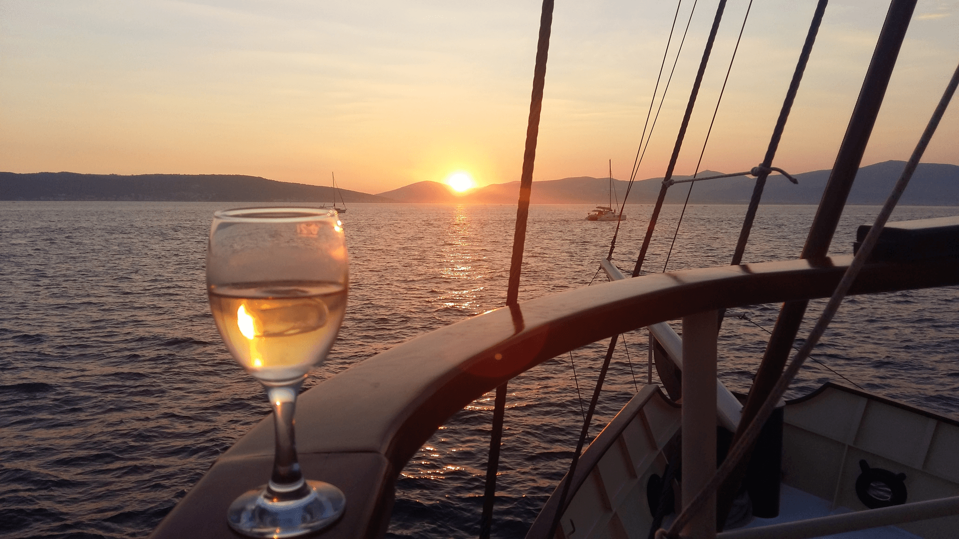 A glass of white wine on the wooden railing of Polaris as the sun sets over the Adriatic near Split