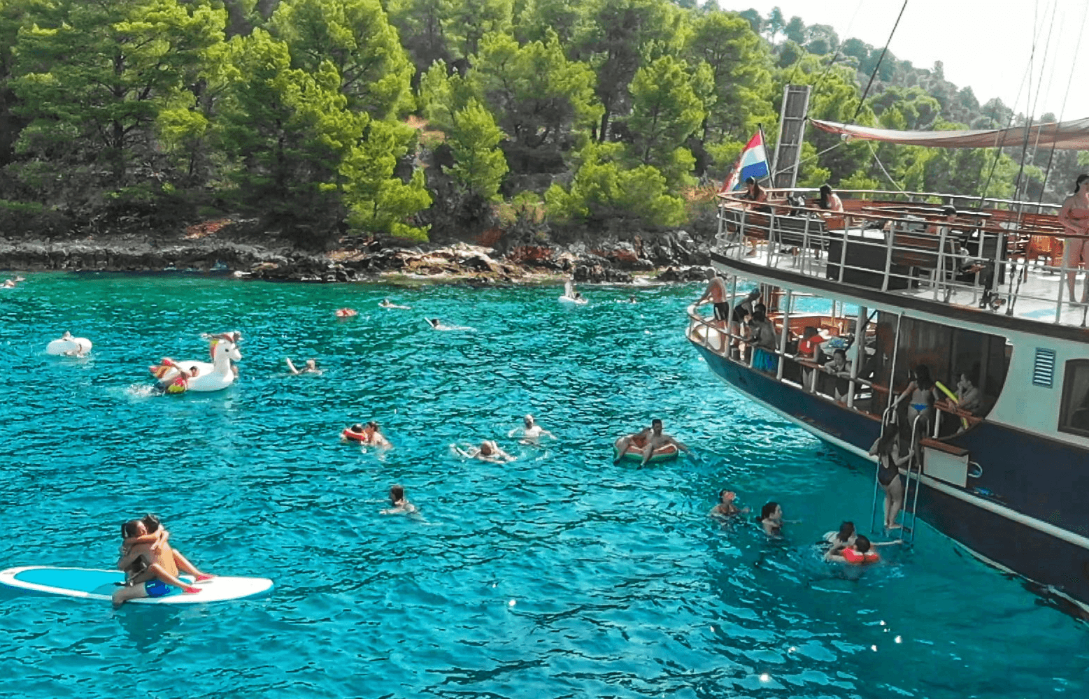 Guests swimming and paddleboarding in a turquoise bay beside the yacht Polaris near Brač and Šolta